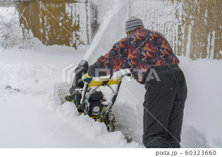 man operating snow blower to remove snow on driveway. Man using a snowblower. A man cleans snow from sidewalks with snowblower 60323660