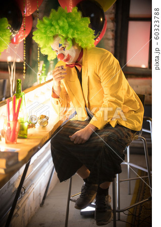 Clown concept - a lost man clown in yellow jacket and green wig sitting in the dressing room and smoking a cigarette after the performance Clown concept - a lost man clown in yellow jacket and green wig sitting in the dressing room and smoking a cigarette after the performance 60323788