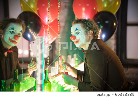 Clown concept - a man sitting in the dressing room and painting a red smile on his face 60323839