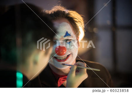 Clown concept - Make-up artist applying paint on the man clown in the dressing room 60323858