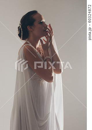 girl in white and with raised hands, attached to the floor dresses. the bride in a dress in Greek style. brunette in pearl jewelry lowered her head. girl in white and with raised hands, attached to the floor dresses. the bride in a dress in Greek style. brunette in pearl jewelry lowered her head. 60324872