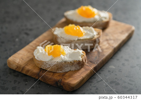 Three ciabatta slices with ricotta and orange marmalade on olive wood board on terrazzo surface Three ciabatta slices with ricotta and orange marmalade on olive wood board on terrazzo surface 60344317