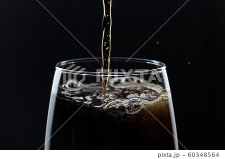 Glass of pouring fizzy drink with ice on a black background Glass of pouring fizzy drink with ice on a black background 60348564