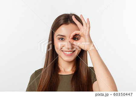 Young woman with ok sign on eye isolate over grey background. Young woman with ok sign on eye isolate over grey background. 60350447