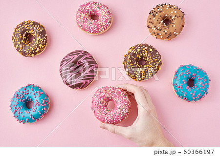 Woman hand take color donut on a pink background. 60366197