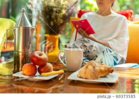 Selected focus of coffee mug with woman relaxing using cell phone on colorful couch. 60373585
