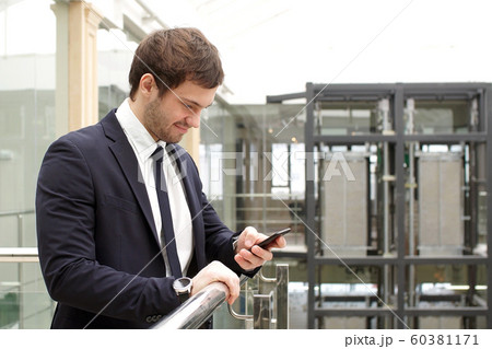 Happy businessman standing in office interior with smartphone in hands 60381171