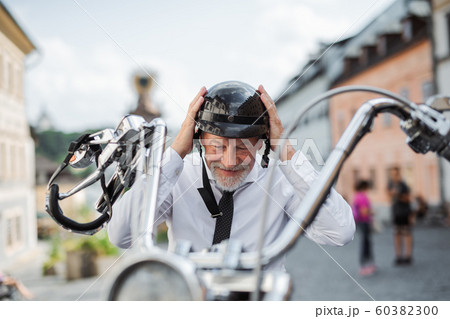 A senior businessman with motorbike in town, putting on helmet. A senior businessman with motorbike in town, putting on helmet. 60382300