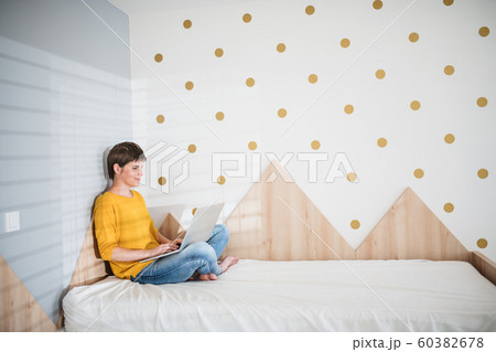 Young woman with laptop sitting on bed in bedroom indoors at home. 60382678