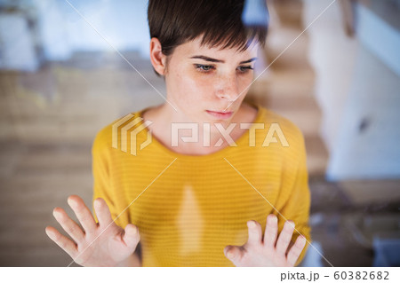 Front view of sad young woman standing indoors at home, hands on glass. Front view of sad young woman standing indoors at home, hands on glass. 60382682