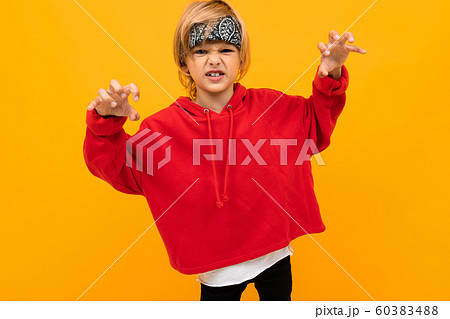 blond boy with a bandana on his head in a red jacket grimaces on an orange background 60383488