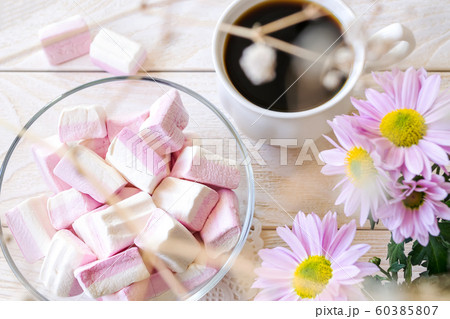 Sweet white pink marshmallows in a glass bowl near cup of hot coffee and pink chrysanthemum flowers 60385807