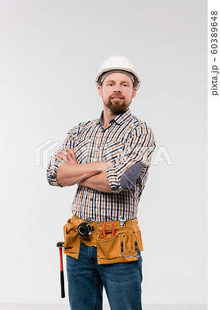 Young technician with toolbelt on his waist crossing arms by chest Young technician with toolbelt on his waist crossing arms by chest 60389648