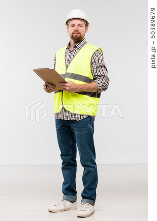 Bearded young engineer with clipboard standing in front of camera in isolation Bearded young engineer with clipboard standing in front of camera in isolation 60389679