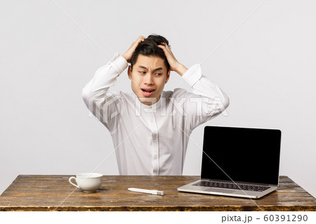 Oh god what have I done. Puzzled and anxious, embarrassed young asian man in shirt, grab head shocked and distressed, staring laptop display, react to embarrassing video posted online 60391290