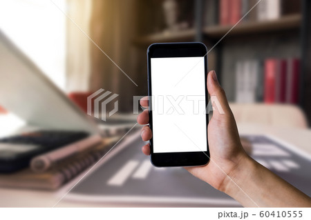 Hand holding white mobile phone with blank white screen in office. Hand holding white mobile phone with blank white screen in office. 60410555