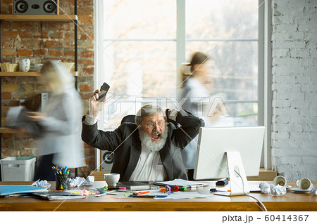 Nervous and tired boss at his workplace busy while people moving near blurred 60414367