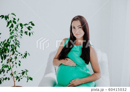 a pregnant woman before childbirth sits in white couch a pregnant woman before childbirth sits in white couch 60415032