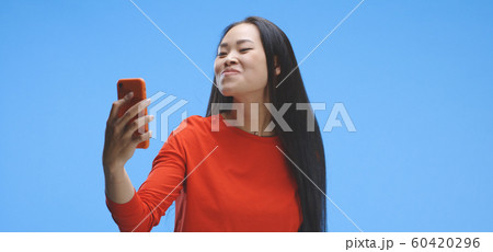 Young woman using smartphone as a mirror 60420296