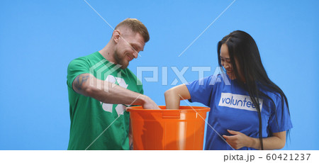 Eco-conscious man and woman putting bottle into bucket Eco-conscious man and woman putting bottle into bucket 60421237