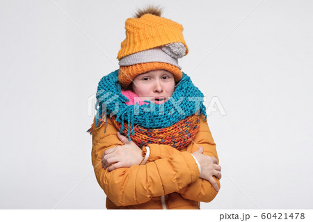Funny young caucasian woman shivering from cold wearing several warm winter hats and scarfs 60421478