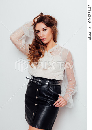 Portrait of a beautiful fashionable woman with hair curls in a white blouse and black skirt Portrait of a beautiful fashionable woman with hair curls in a white blouse and black skirt 60423882