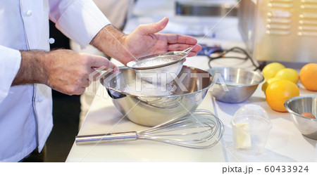 Pastry chef Baker sieving flour into a bowl in the Pastry chef Baker sieving flour into a bowl in the 60433924