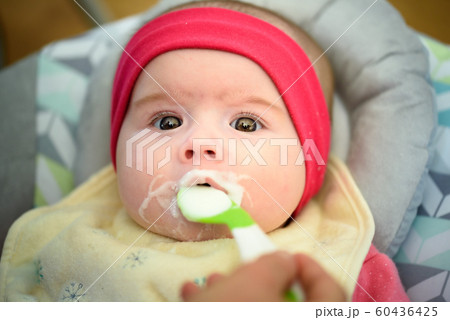Mother feeding hungry five month old baby with spoon, solid food. Newborn feeding concept 60436425