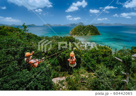Zipline over Las Cabanas Beach with tourist on sunny day with white clouds over sea. El Nido, Palawan, Philippines Zipline over Las Cabanas Beach with tourist on sunny day with white clouds over sea. El Nido, Palawan, Philippines 60442065