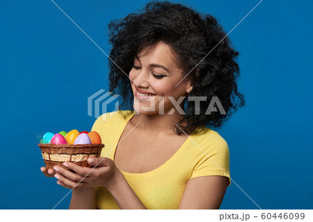 Smiling woman holding a basket with colorful Easter eggs Smiling woman holding a basket with colorful Easter eggs 60446099