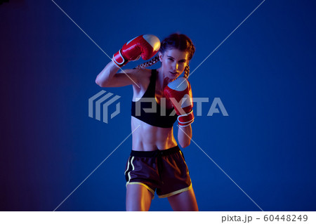 Fit caucasian woman in sportswear boxing on blue studio background in neon light 60448249