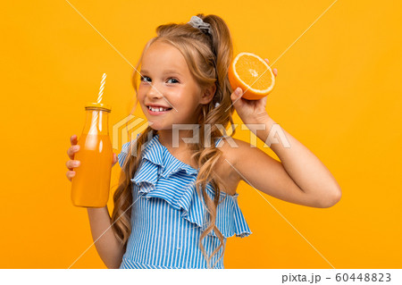 funny girl holding a sliced orange and a bottle of juice in her hands on a yellow background 60448823