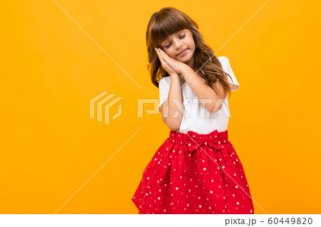 Caucasian girl in a skirt shows that she wants to sleep on a yellow background 60449820