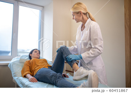 Blond doctor wearing sterile gloves working with patients leg Blond doctor wearing sterile gloves working with patients leg 60451867