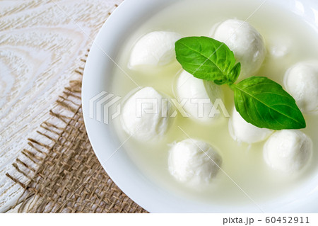Close-up of bowl with mini mozzarella cheese balls in a brine and basil. Close-up of bowl with mini mozzarella cheese balls in a brine and basil. 60452911