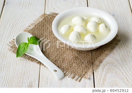 White bowl with small mozzarella cheese balls in a brine and porcelain spoon. White bowl with small mozzarella cheese balls in a brine and porcelain spoon. 60452912