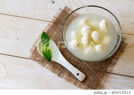 Glass bowl with mini mozzarella cheese balls in a brine and porcelain spoon on a white wooden table Glass bowl with mini mozzarella cheese balls in a brine and porcelain spoon on a white wooden table 60452913