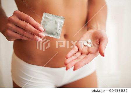 Contraception. Safe sex, choosing a contraceptive. Sexy girl with a condom and pills in her hands Contraception. Safe sex, choosing a contraceptive. Sexy girl with a condom and pills in her hands 60453682