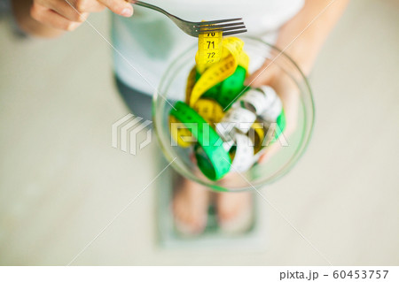 Diet and Weight Loss. Woman holds bowl and fork with measuring tape Diet and Weight Loss. Woman holds bowl and fork with measuring tape 60453757