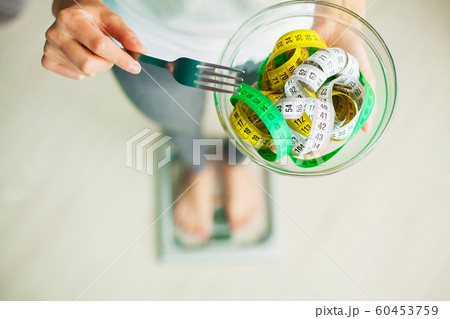Diet and Weight Loss. Woman holds bowl and fork with measuring tape 60453759