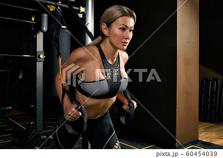 Front view of confident young blonde woman doing weight lifting workout Attractive young woman lifting weight looking forward Strong trained body shape arms chest legs. Front view of confident young blonde woman doing weight lifting workout Attractive young woman lifting weight looking forward Strong trained body shape arms chest legs. 60454039