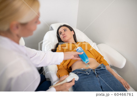 Female doctor applying gel for ultrasound procedure on patients belly 60466761