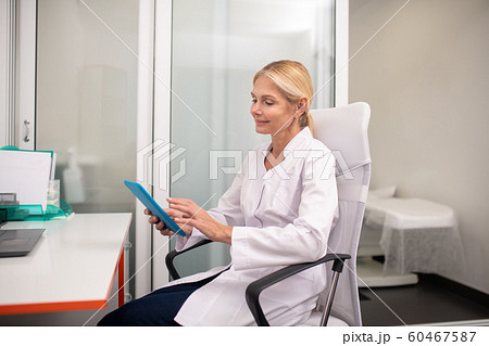 Blond pleasant doctor with tablet in her hand looking interested 60467587