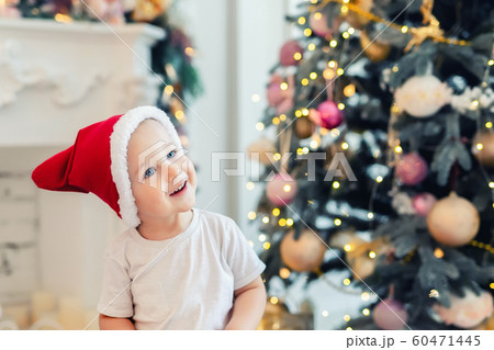 Adorable cute child boy having fun playing at home in red santa claus hat and festive christmas tree on background. Happy toddler kid looking ,smiling and dreaming for holiday gift, wonder an miracle 60471445