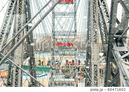 aerial red cabin view and steel frame construction of oldest ferris wheel in Vienna Prater amusement fair park during cold snowy winter day. Snowfall blizzard weather in european city 60471602