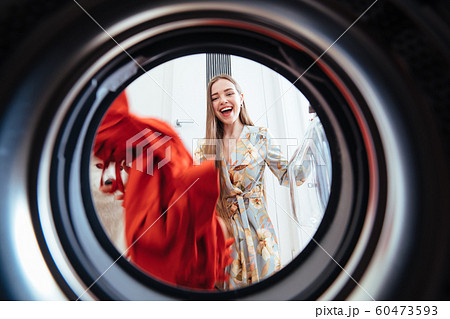 Young woman at home puts the dress in the drying machine. 60473593