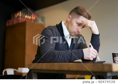 Pensive man with tablet in hands sitting at table 60474539