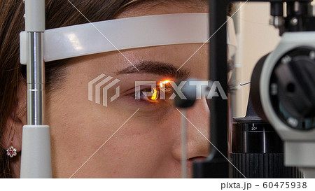 Ophthalmology treatment - a young woman checking her visual acuity with a light of special big optometry machine - brown eyes color Ophthalmology treatment - a young woman checking her visual acuity with a light of special big optometry machine - brown eyes color 60475938