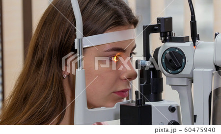 Ophthalmology treatment - a young woman checking her visual acuity with a light of special big optometry machine Ophthalmology treatment - a young woman checking her visual acuity with a light of special big optometry machine 60475940