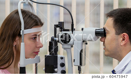 Ophthalmology treatment - young woman checking her visual acuity with a special equipment in the bright cabinet Ophthalmology treatment - young woman checking her visual acuity with a special equipment in the bright cabinet 60475947